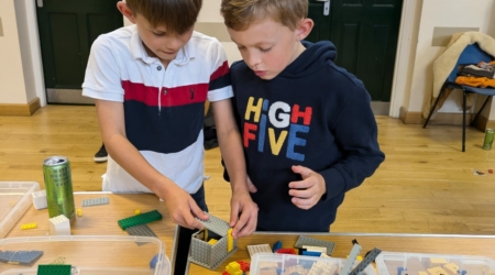 Two boys playing with boxes of lego on big tables inside Coggeshall Village Hall