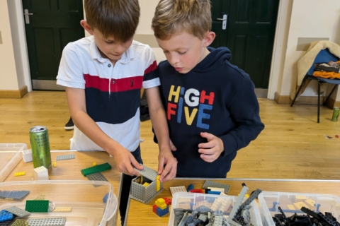Two boys playing with boxes of lego on big tables inside Coggeshall Village Hall